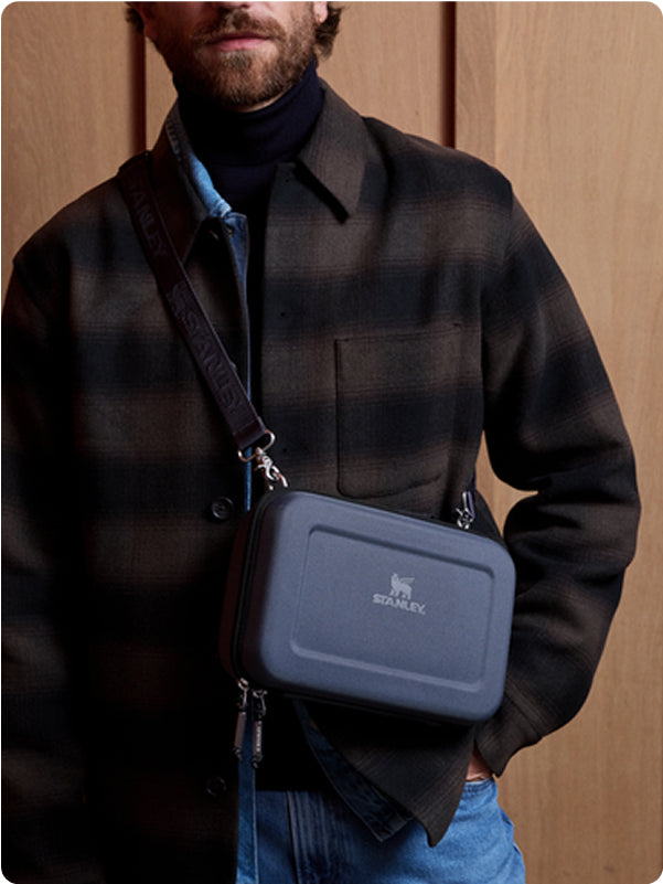 Stanley 1913 navy hard-shell lunch box worn as a crossbody bag over a plaid jacket