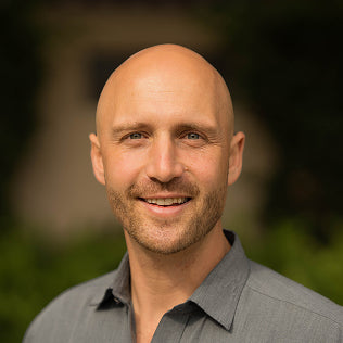 Smiling bald man in a gray shirt photographed outdoors with a soft green background