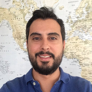 Stanley 1913 branded blue polo shirt worn by a smiling man standing in front of a world map backdrop.