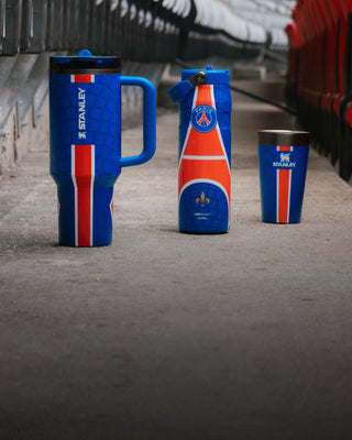 Stanley 1913 PSG-edition tumbler, water bottle, and cup in blue and red stripe design, displayed in stadium tunnel.