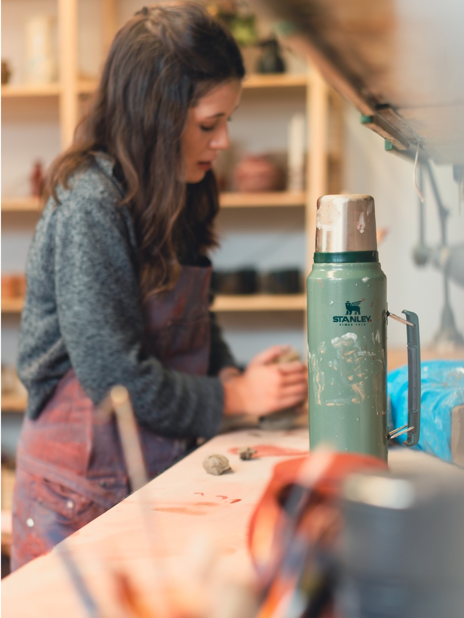 Stanley 1913 Classic Legendary Bottle in Hammertone Green, paint-splattered, on a pottery studio workbench